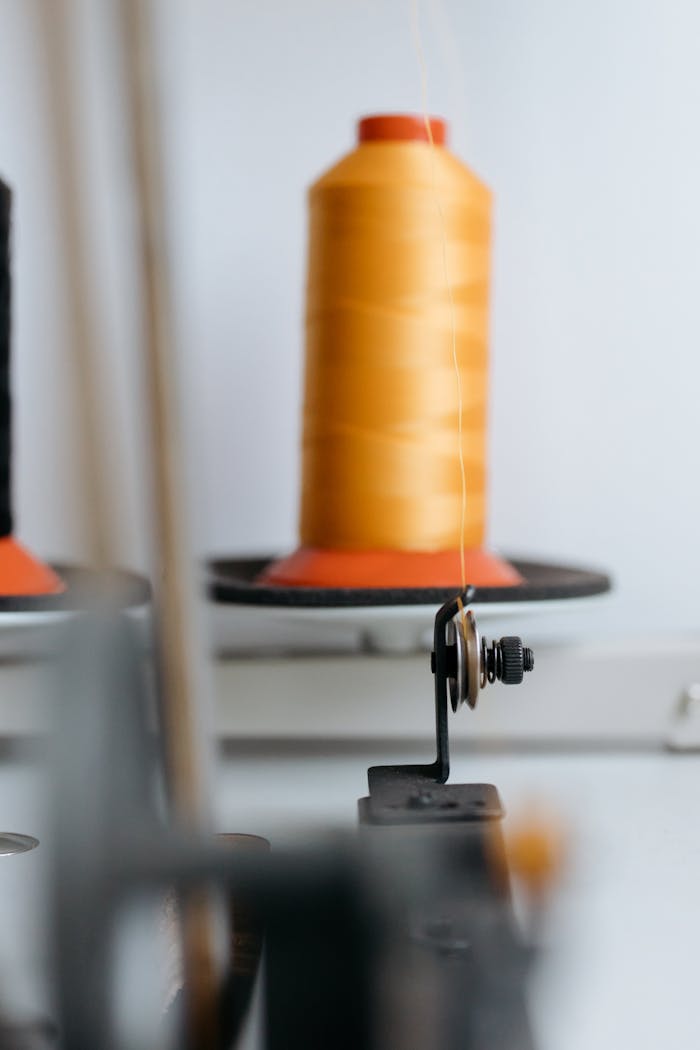 Detailed view of sewing machine with orange thread bobbin, showcasing craft and machinery.